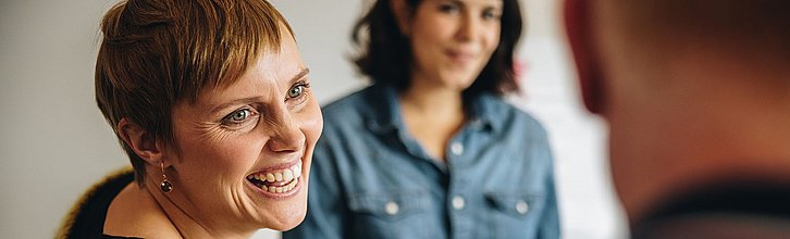 Lachende Person, im Hintergrund zwei weitere Personen zu sehen