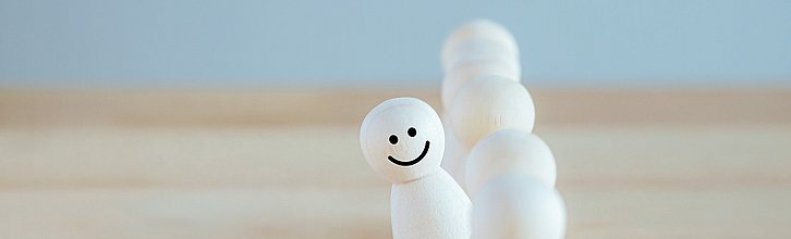 Spielfiguren, eine hat ein Gesicht aufgemalt und schaut aus der Reihe